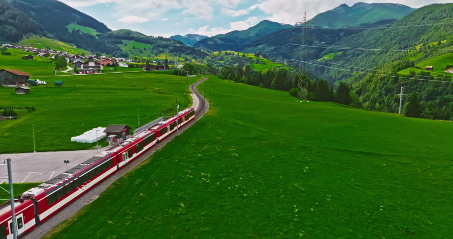 Establishing shot of Switzerland. Aerial view of the green meadows of Switzerland, with the Alps and clouds in the background