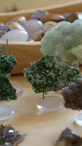Vertical video: Panning camera revealing green mineral cluster on wood table, showing lilac texture. Botryoidal, druzy, lavender, crystal, surface, minimalist, vertical video