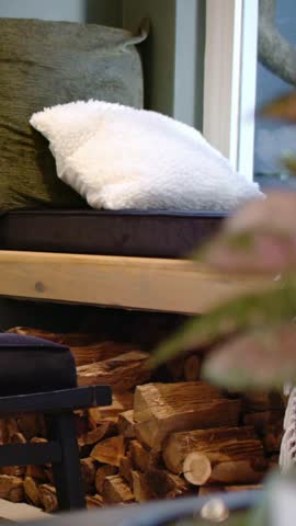 Vertical video: Framing white pillow as camera drifting to bench by window, revealing firewood. Cushion, cozy, nook, sunroom, texture, greenery, vertical video