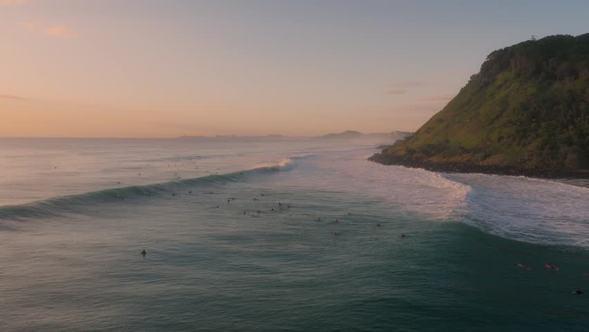 People Surfing Next To Burleigh Headland At Sunrise In Gold Coast, QLD, Australia. - aerial shot
