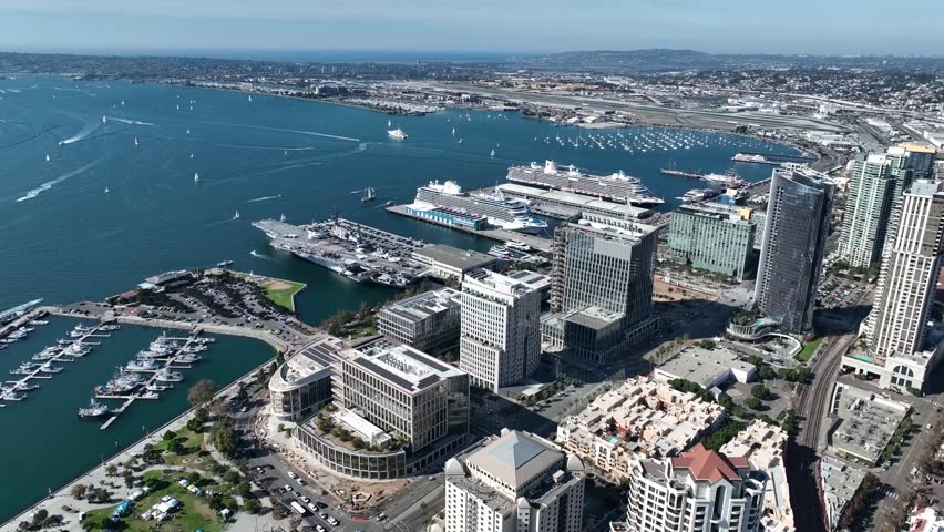 Cinematic high-angle drone shot looking over the USS Midway aircraft carrier, cruise ships, and San Diego Bay.