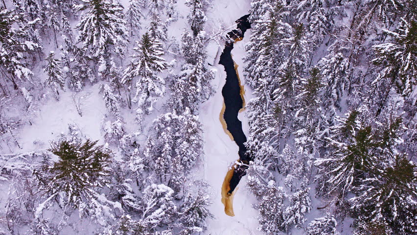 Winter aerial footage of Canyon Falls waterfall flowing through a snow-covered forest landscape.