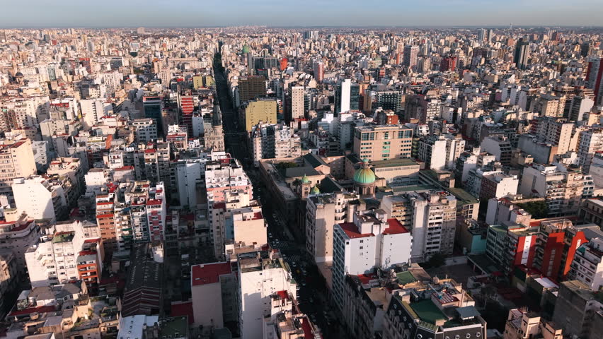 Major avenue cuts through the dense urban fabric of Buenos Aires, Argentina, lined with residential towers, commercial buildings and continuous city blocks, slow orbit drone shot.