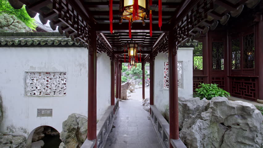 A narrow corridor with hanging lanterns leads to a lush garden, showcasing traditional Chinese architecture. Ideal for cultural documentaries or travel features.