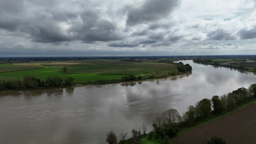 Trebbia River with flooded banks and farmland capturing the Po Valley landscape under overcast sky, Drone push forward