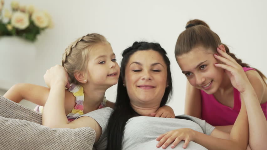 Two girls kissing their pregnant mother

