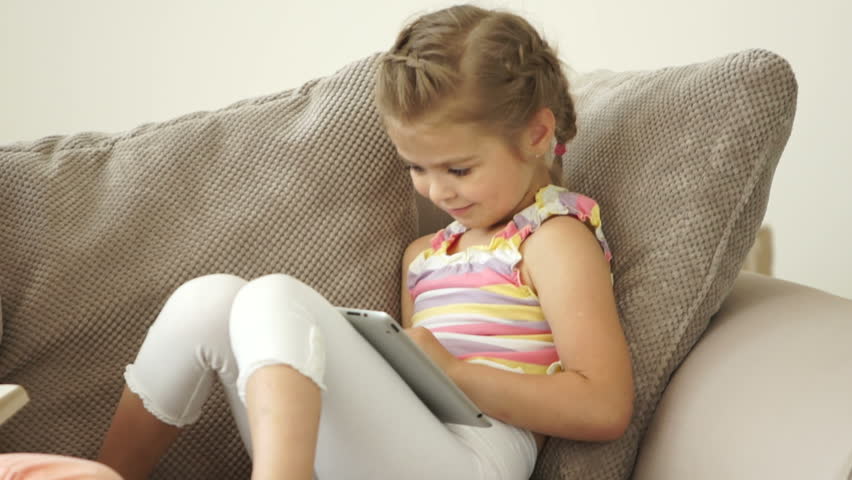 Two sisters sitting on sofa with book and tablet pc
