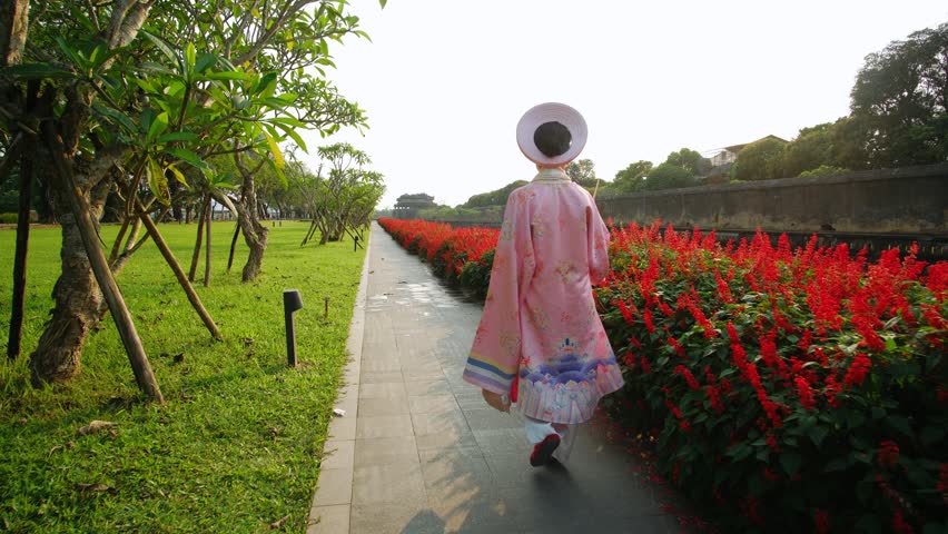 Vietnamese woman wearing traditional dress walking in a garden in hue imperial citadel, vietnam.