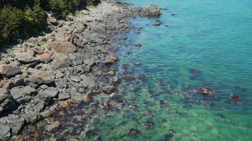 Rugged boulders along rocky shore meeting crystal-clear turquoise water at Haeundae Blue Line Park coast in Busan South Korea