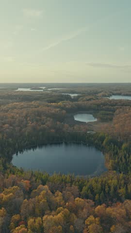 High aerial parallax reveals vast Wisconsin autumn landscape near Balsam Lake with multiple lakes scattered across golden fall forest under morning sky