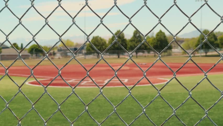 Shallow depth of field shot featuring a sharp chain link fence with an empty baseball diamond softly blurred behind it.