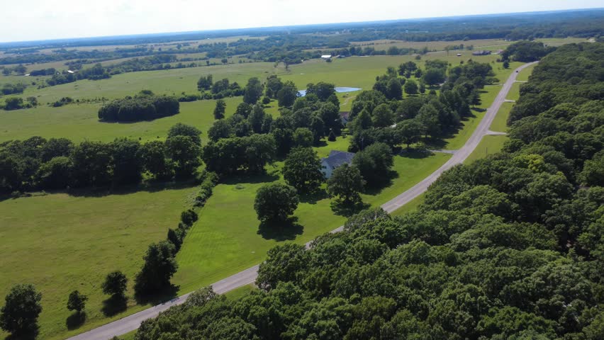 Drone footage of a rural road near Stockton Lake, Missouri, passing between wooded Ozark hills, homes, open fields, and countryside.