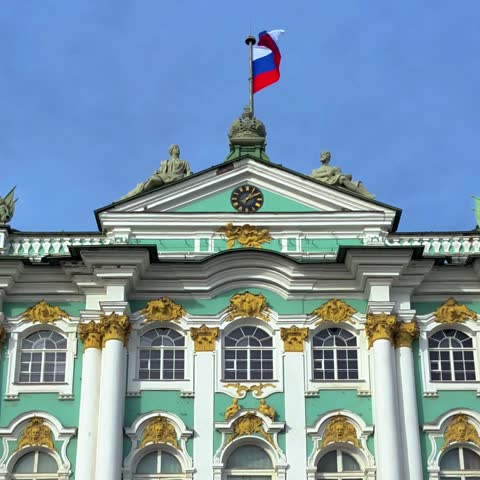 Central view of the Winter Palace and the State Hermitage Museum on Palace Square in Saint Petersburg, Russia, with the Russian flag waving above the historic landmark
