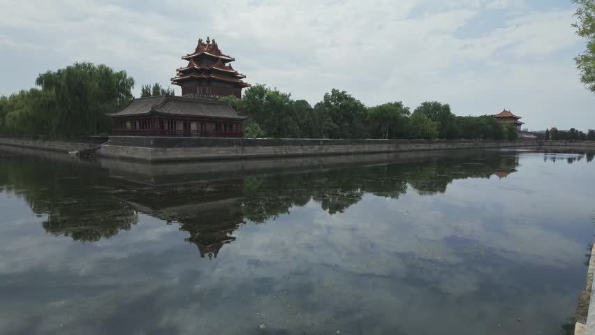 Scenic panning shot of the historic Forbidden City corner tower and its reflection on the calm moat water in Beijing.