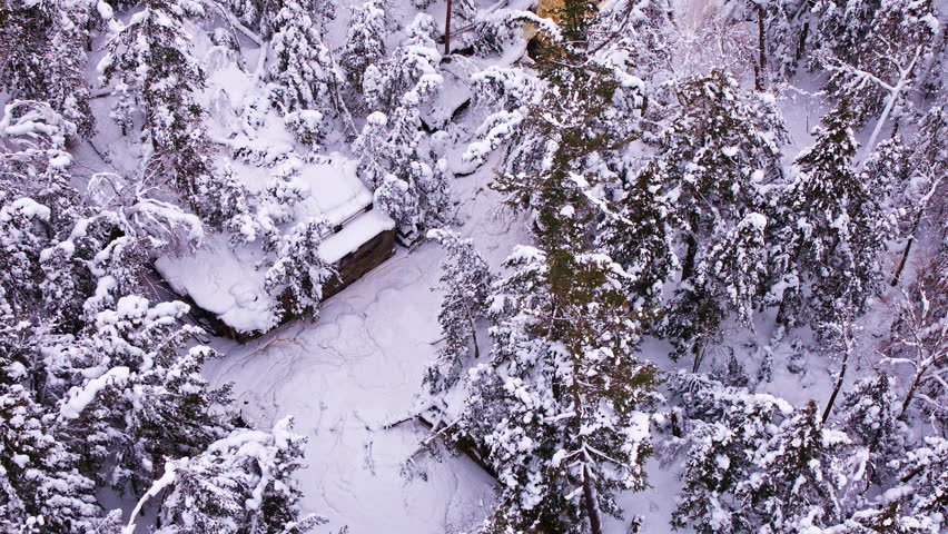 Aerial drone footage of Canyon Falls waterfall partially iced over amid a winter landscape in northern Michigan.