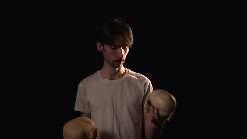 Serious young man holding two human skulls in dramatic studio lighting