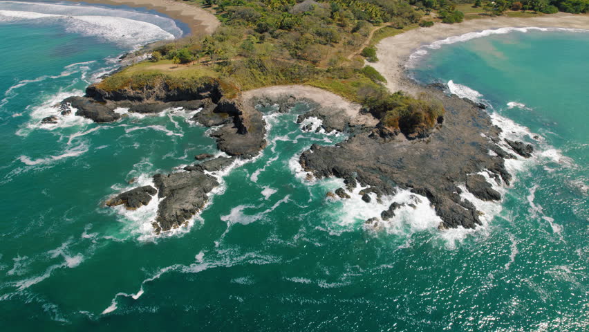 Rocky peninsula with ocean waves hitting the shore on a sunny day in Costa Rica