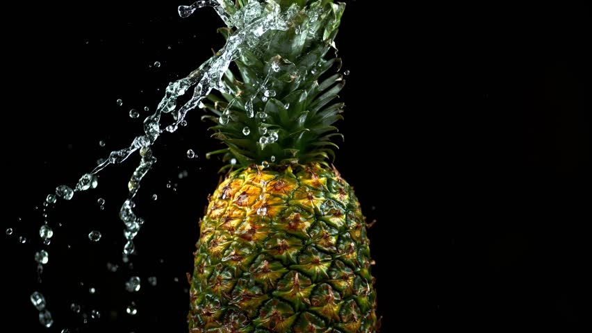 Fresh pineapple splashes into water in slow motion, creating dramatic droplets on a black background.