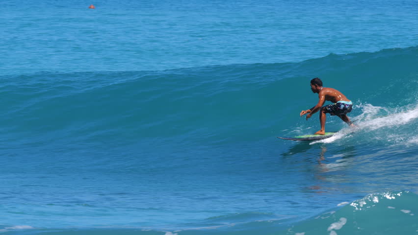 SLOW MOTION, CLOSE UP: Skilled surfer makes a smooth carving turn on a clean blue wave under bright tropical light. Surfing perfect waves in the tropical Mentawai Islands, iconic surfing paradise.