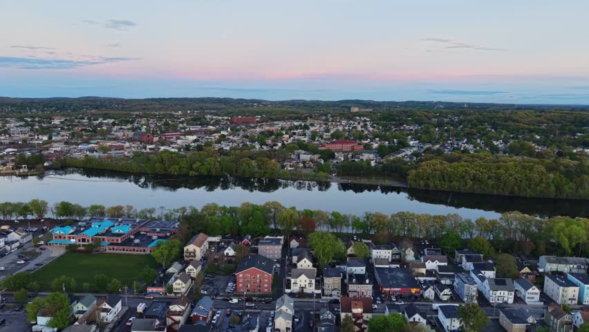 Merrimack River and city skyline at dusk in Lawrence, USA. Aerial forward, copy space