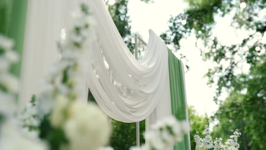 A romantic wedding arch made of white roses and green tulle before the bride and groom ceremony. Decor and floristry	