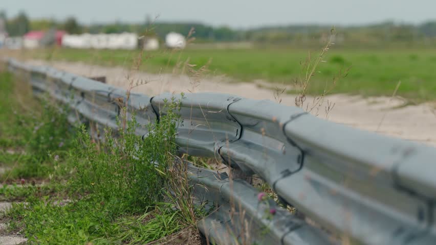 Static shot of a metal barrier along the side of a dragstrip, overgrown with grass and weeds moving in the wind.