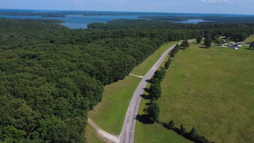 Drone footage of a rural road near Stockton Lake, Missouri, with forest, open fields, distant lake views, and an Ozark bridge on the horizon.