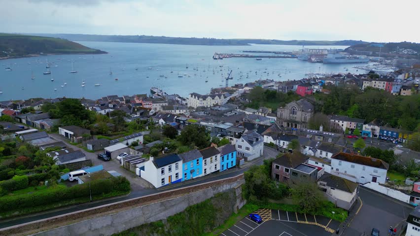 Aerial drone view of Falmouth Harbour featuring waterfront homes coastal townscape marina facilities and Fal Estuary waters stretching beneath dramatic cloudy skies