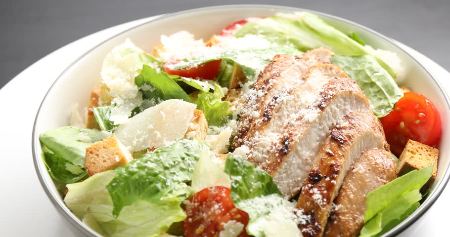 Tasty Caesar salad with chicken on black table, rotating