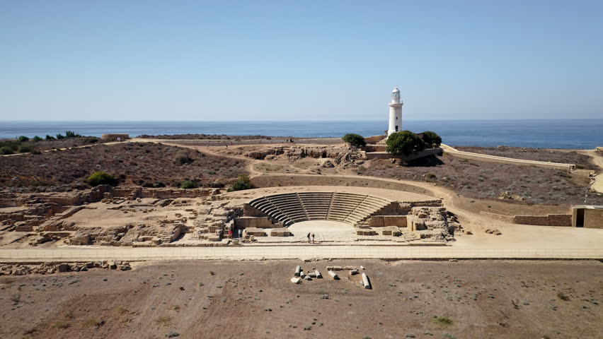 Ancient Roman Odeon and historic Paphos Lighthouse standing along the Mediterranean coastline, showcasing an important archaeological site in Cyprus under a clear sky. Aerial view drone flight