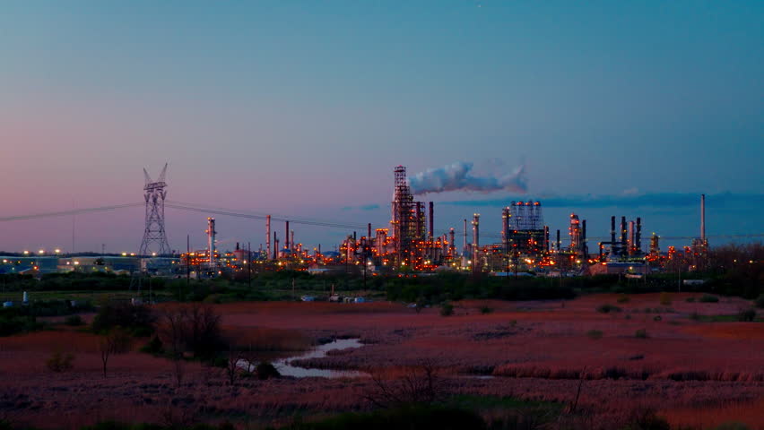 Large electrical pylon and high-voltage power lines adjacent to an illuminated petrochemical manufacturing facility in Joliet, Illinois, USA