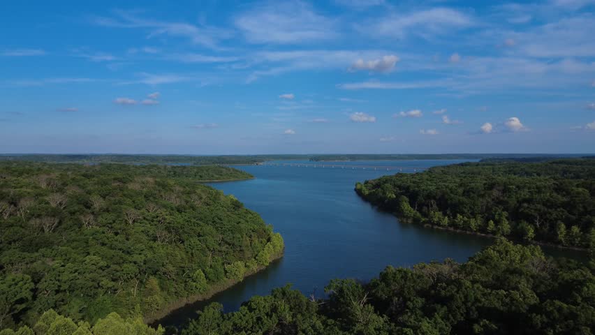 Drone footage over Stockton Lake, Missouri, showing open blue water, wooded coves, Ozark shoreline, distant bridge, and summer sky.