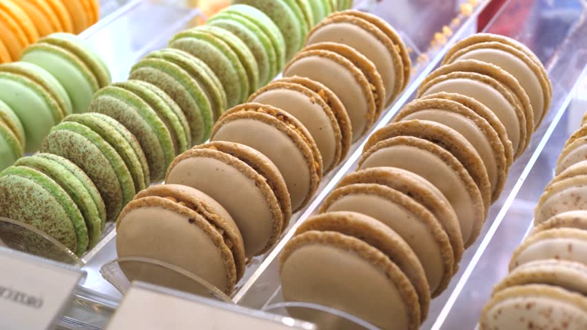 Delicious and colorful french macarons sitting in rows inside a bakery display case, showcasing various flavors like pistachio, chocolate, and coffee for sale at a local sweet patisserie