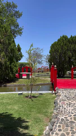 Japanese Pond Garden With Red Bridge Stone Path Green Trees And Clear Blue Sky