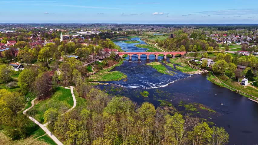 Wide drone view of Kuldīga showing the historic brick bridge, wide river rapids, and old town. Kuldīga, Latvia.