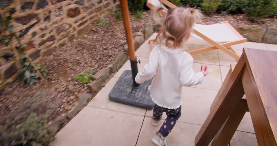 Toddler girl moving across the patio outside a family home. Everyday childhood moment in a domestic outdoor space