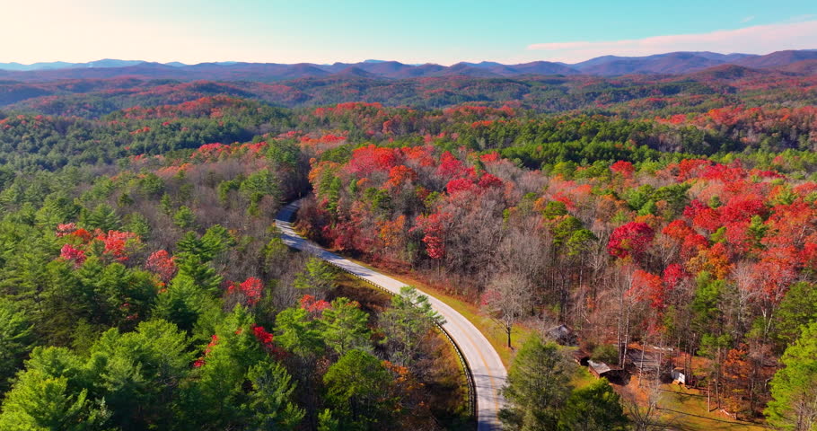 Car cruising on scenic road in Appalachian mountains at sunset. Trees glowing in vibrant fall foliage as the sun sets.