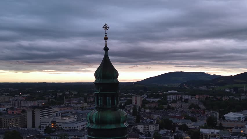 Historic Salzburg skyline at sunset beneath dramatic storm clouds. The iconic church tower rises above the city center while the last light of day illuminates the horizon. Scenic urban landscape in Austria, showcasing historic architecture, culture, tourism, and atmospheric weather conditions.
