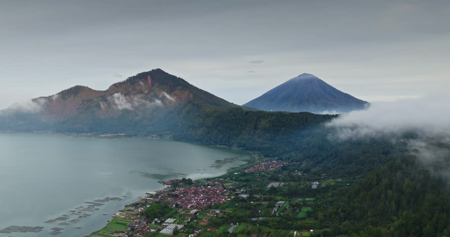 Mount Batur and Lake Batur forming a caldera while low clouds covering the sides of Mount Batur with Mount Agung rising from the mist in Kintamani, travel and explore Bali. Aerial view drone flight