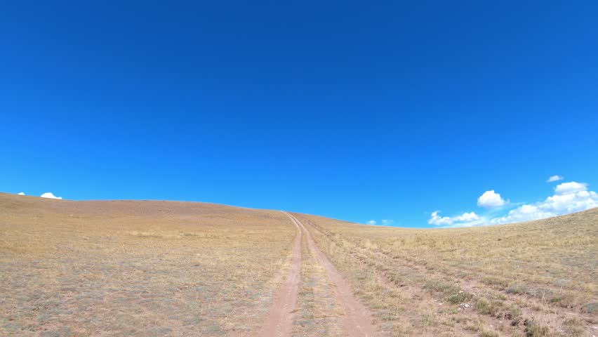 Video of a car driving along a country road under blue sky. Altai desert and semi-desert environment.