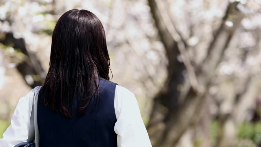 A portrait of a high school girl smiling under a row of cherry trees.