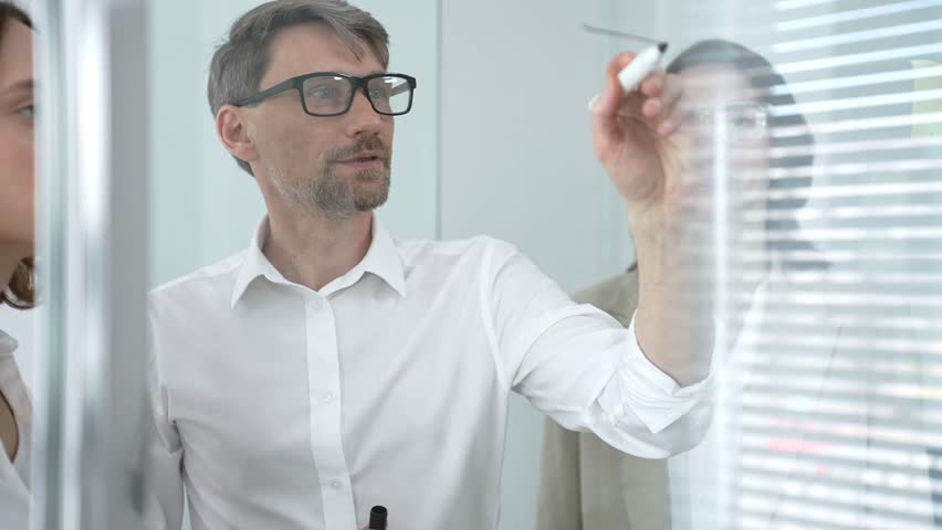 Business colleagues collaborating on a glass board in an office, discussing strategy, sharing ideas, and brainstorming during a productive meeting for project development