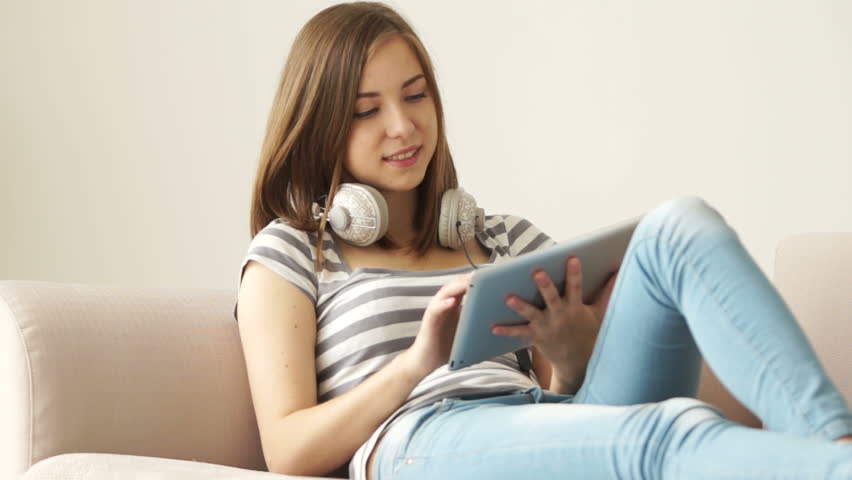 Girl with headphones sitting on couch and chatting on tablet pc
