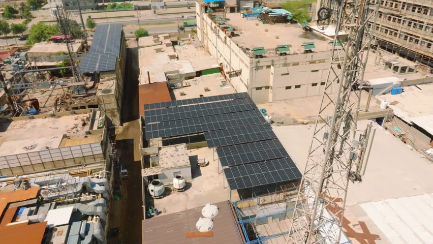 Large solar panel installation on a factory roof within a dense manufacturing district of Karachi. Aerial orbit looking down.