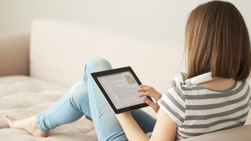 Girl sitting on sofa with tablet pc and looking at camera
