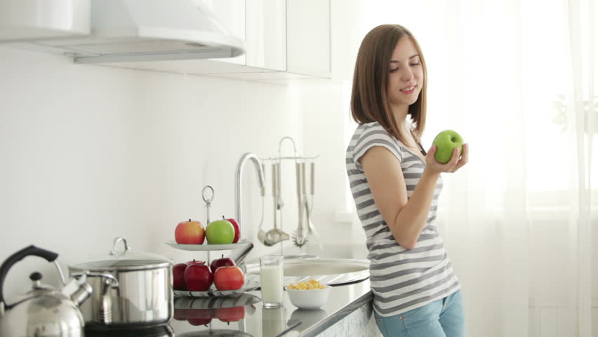 Girl standing in kitchen and bitting juicy apple
