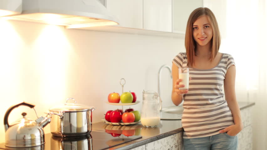 Young adult stands in the kitchen and drinking milk
