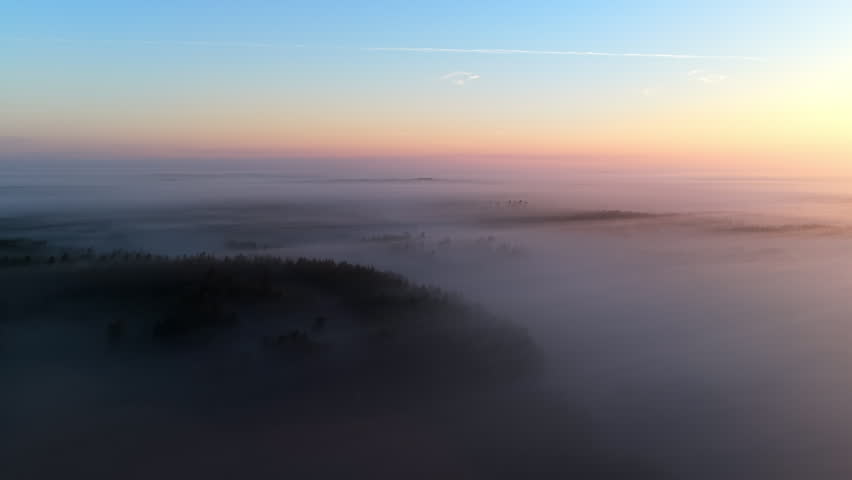 Mystical aerial view of layers of fog over the woods under a vivid twilight sky