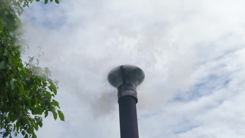Smoke comes out of a sauna chimney against a cloudy sky on a summer day. Close-up of a country house chimney with rising plumes of white smoke