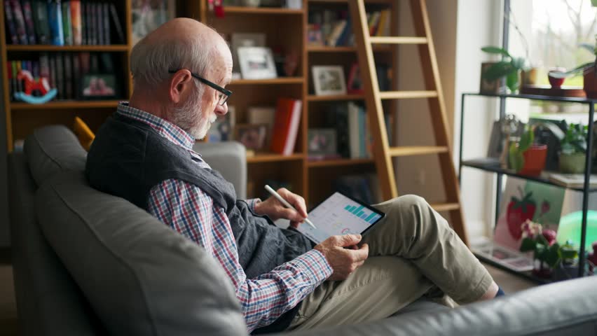 Elderly man relaxing in cozy living room at home, using tablet.